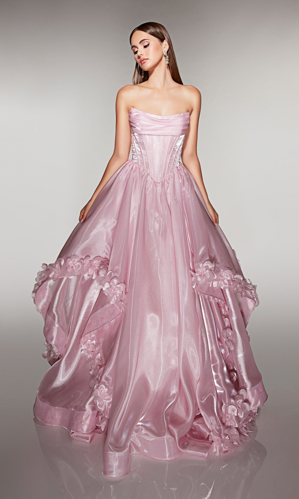 A woman wears the pink Long Prom Dress: Alyce 62014, a strapless ballgown made of liquid organza with 3D floral appliques and a full skirt, posed against a plain background.